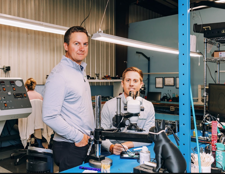 Two Soundtrace team members at an electronics workbench with a microscope and testing equipment.